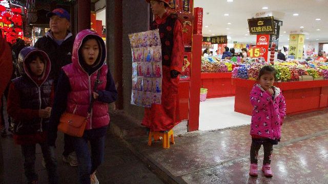 Children walk past by a man dressed like an emperor, center, promoting photography services in Beijing on Thursday. The official Xinhua News Agency says China’s ruling Communist Party has decided to abolish the country’s one-child policy and allow all couples to have two children. (AP Photo/Ng Han Guan)