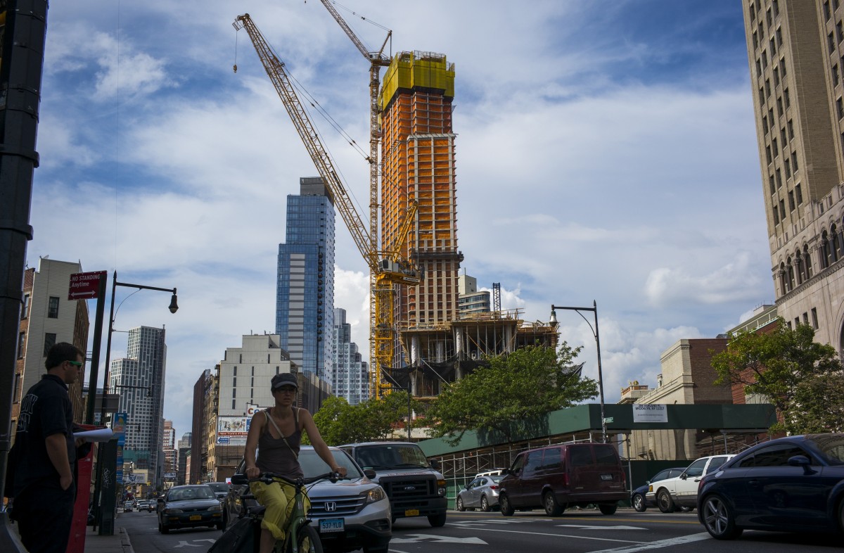 A woman bicycles past a 52-story apartment building under construction in downtown Brooklyn on Aug. 23. New York City is failing to increase its housing supply enough to meet demand. (Photo by Robert Nickelsberg/Getty Images)